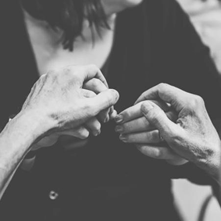 Black and white photo of a pair of hands over another woman’s hands. Hand over hand ASL.