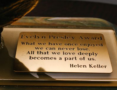 A zoomed in photo of the plaque on top of the Evelyn Presley Award. It reads: Evelyn Presley Award - What we have once enjoyed we can never lose. All that we love deeply becomes a part of us. Helen Keller